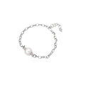 Rhodium-plated silver chain bracelet with single white freshwater pearl and heart charm clasp on cream background