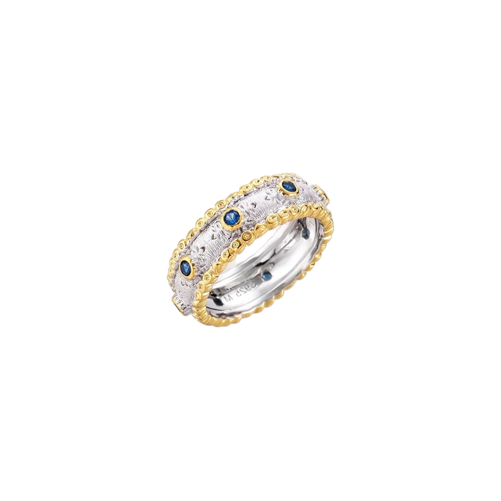 Two-tone ring with brushed silver center, gold beaded edges, and blue zirconia stones on white background.