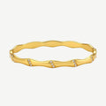 Gold-toned wavy bangle with bamboo-style segments and CZ crystal clusters on cream background. 18K plated stainless steel.