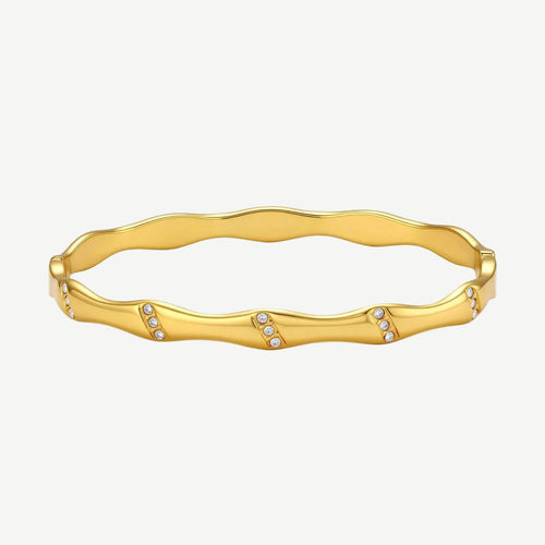 Gold-toned wavy bangle with bamboo-style segments and CZ crystal clusters on cream background. 18K plated stainless steel.