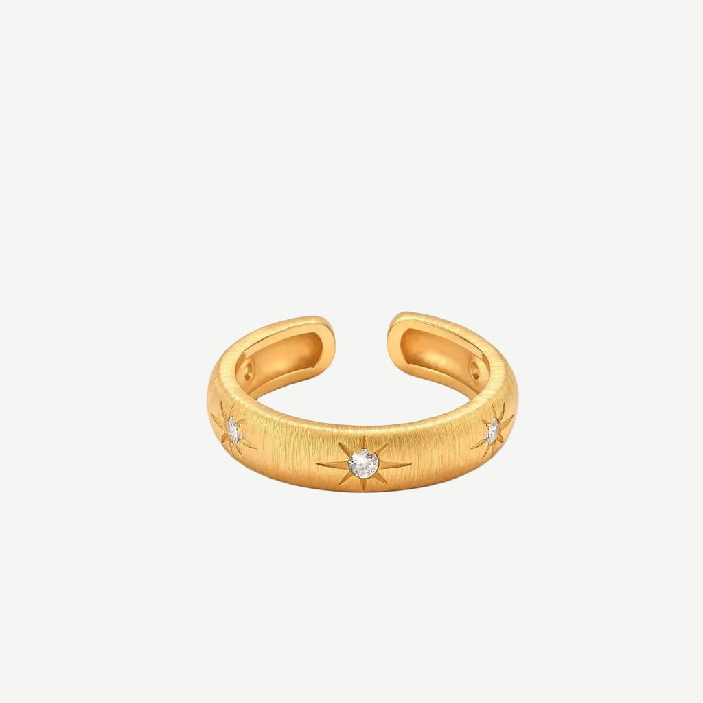 Gold open-band cuff ring with brushed matte finish, engraved 8-point star motifs, and round CZ stones on white background.